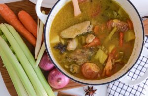 A pot of chicken soup with vegetables and herbs in a side