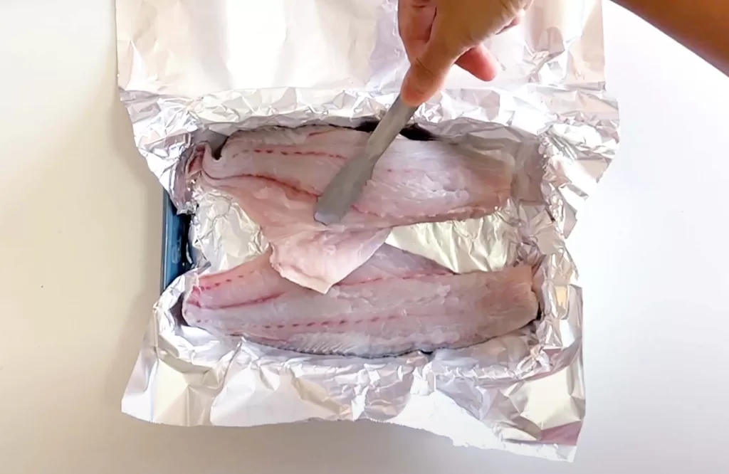 Placing fish fillet in a baking dish with aluminium foil