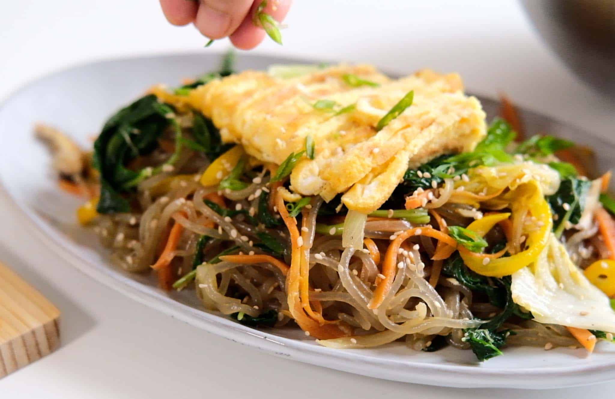 Japchae with egg topping garnished with sesame seeds and scallions