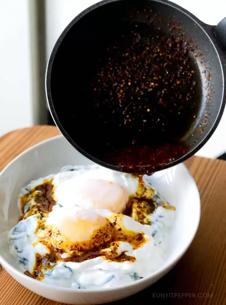 Pouring chili oil from pan onto poached egg and spinach yogurt