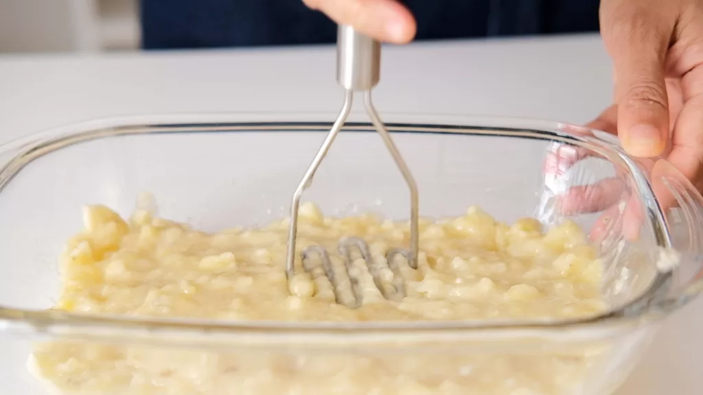 Step 2.1 on how to make gingerbread bundt cake: The photo shows me mashing bananas using masher and showing the texture of the mashed banana