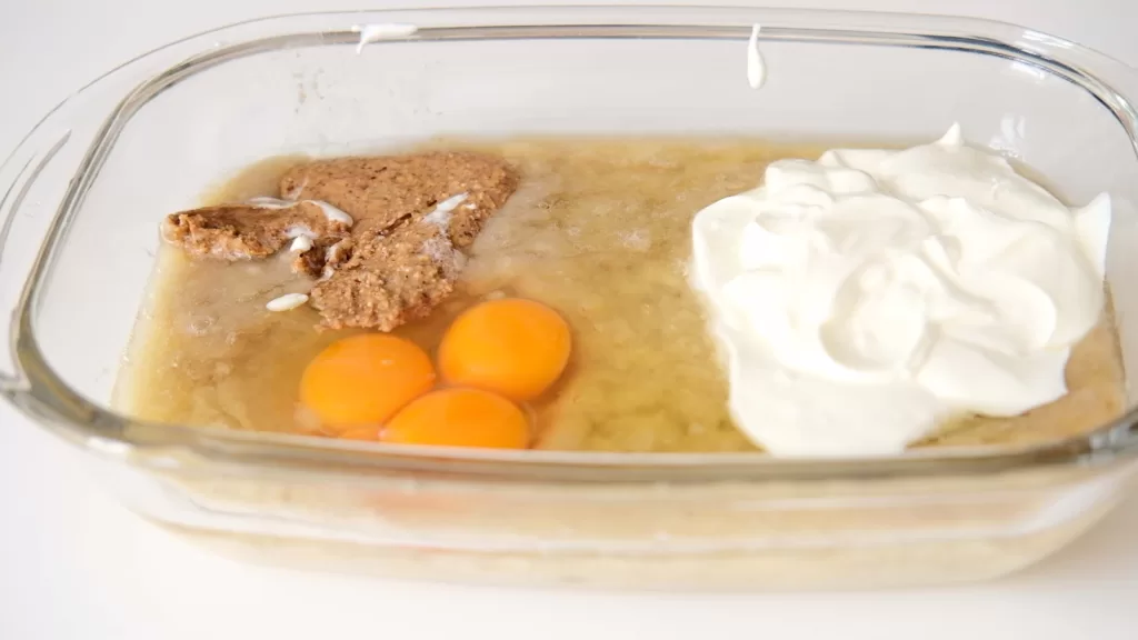 A bowl of mashed banana with wet ingredients; eggs, greek yogurt and almond butter