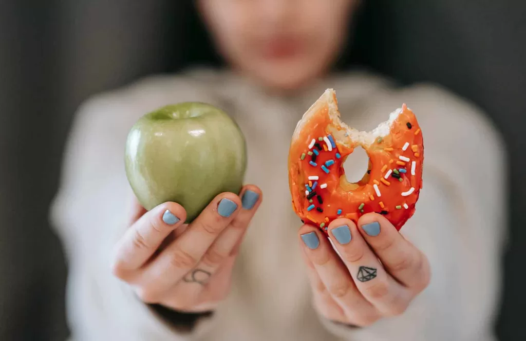 Highly processed food to fresh food. Women holding apple and doughnut