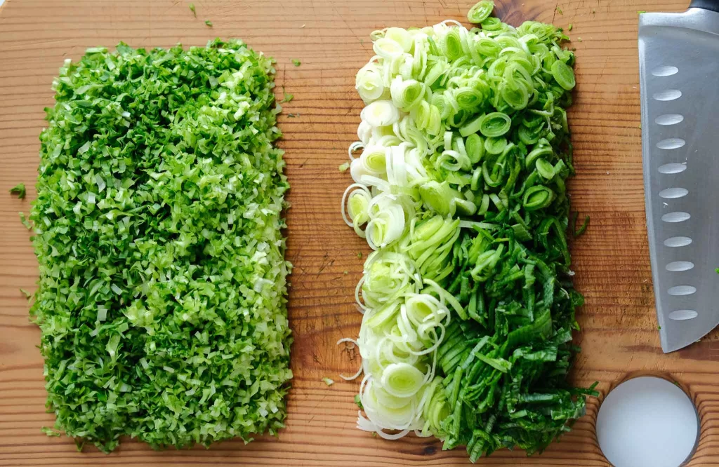 Thinly chopped leeks and chives in a cutting board