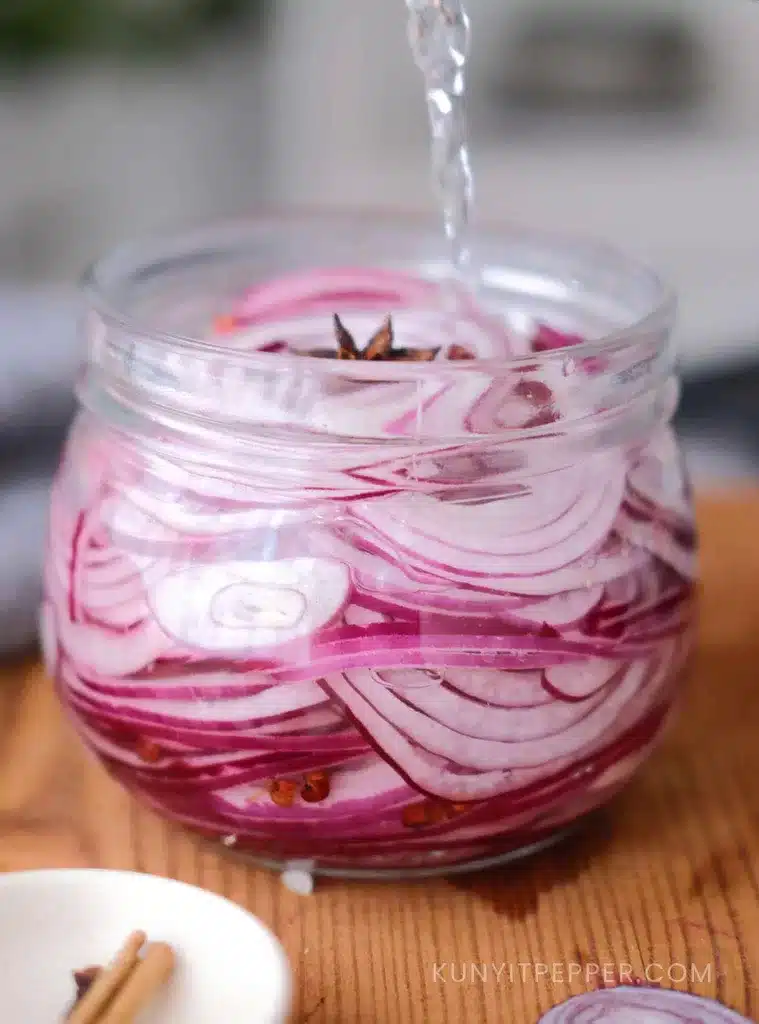 Pouring brine into a jar of red onions and spices