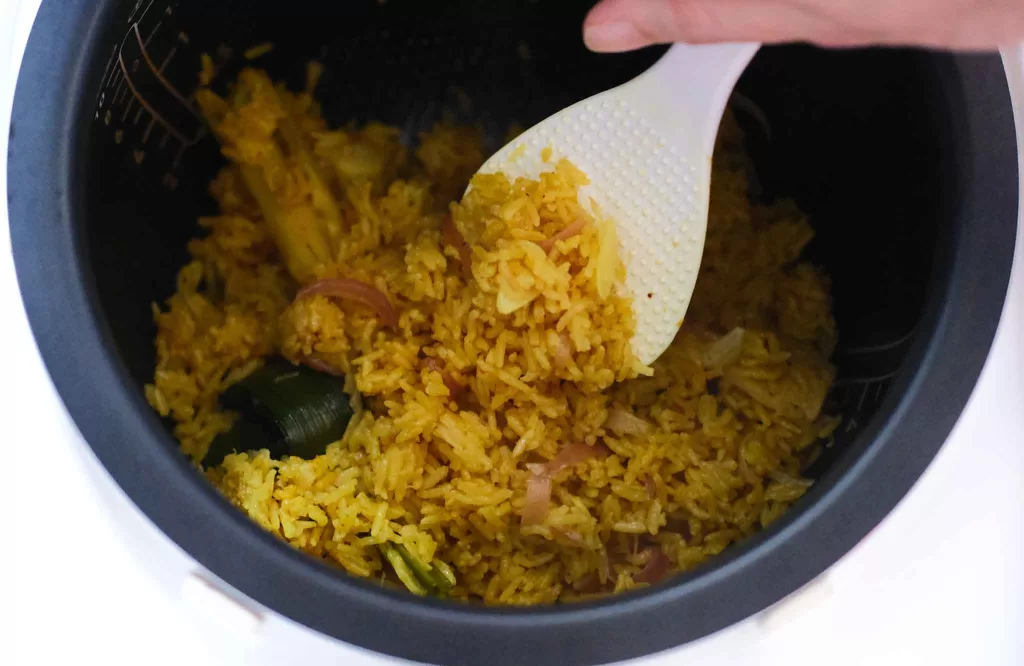 Fluffing cooked Indonesian yellow rice in a rice cooker