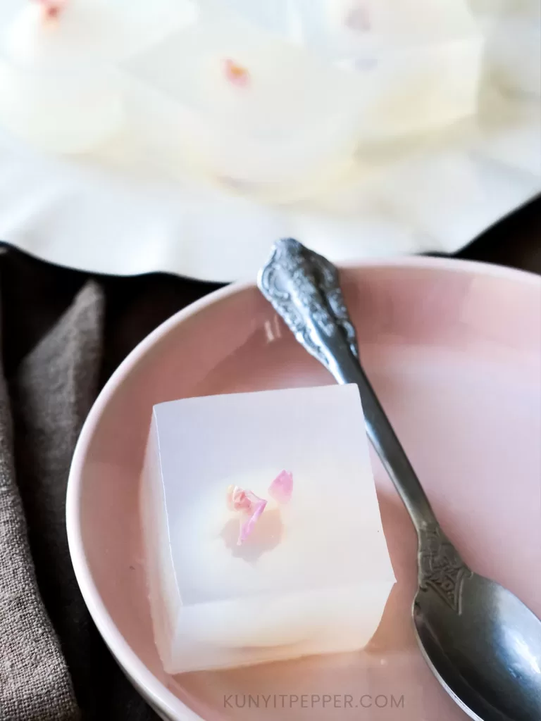 A cube-size of lychee coconut jelly in a dish next to a spoon
